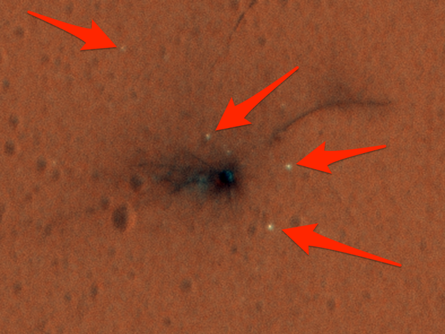 A mancha preta é o local onde a sonda Schiaparelli Mars, da Agência Espacial Européia, caiu.  As manchas brancas, apontadas com flechas, são pedaços da sonda.
