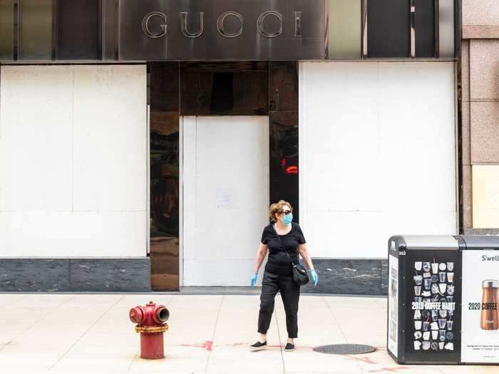 A woman wearing a blue face mask and gloves prepares to hail a cab in front of a boarded-up Gucci store on July 8 in Chicago.